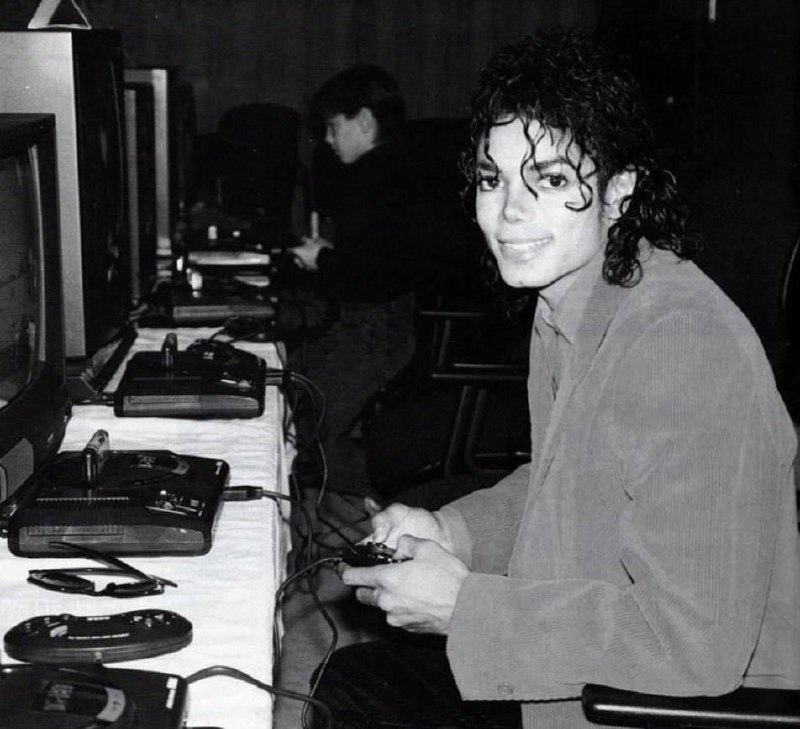 #名人 这张照片展示了迈克尔·杰克逊在1980年代，坐在电视机前玩**世嘉Mega Drive（Sega Genesis）**的画面