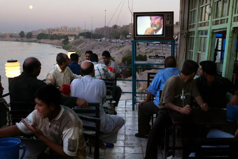 ↩️🖼 伊拉克人在底格雷斯河畔的一家咖啡馆里观看萨达姆·侯赛因的审判