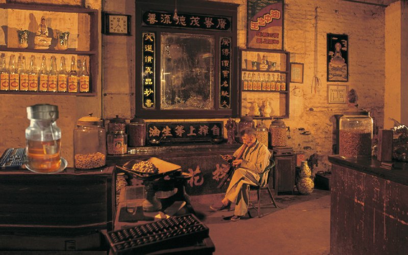 1970年代的香港，一位店主在传统中式店铺中悠闲地抽着烟斗
