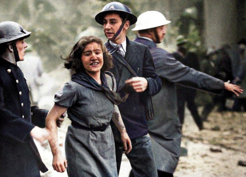 这位微笑的女孩，虽然满身灰尘但显然没有受伤，1940年在伦敦街头被人搀扶着过马路，她刚从一栋被炸弹炸毁的建筑废墟中获救 #二战