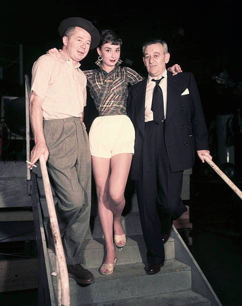 #名人 1954 年 1 月 1 日，奥黛丽·赫本在派拉蒙影业和导演她的好莱坞电影的两名男子之间摆出漂亮的姿势