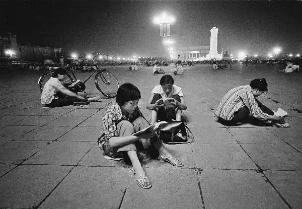 1981年中国改革开放初，天安门广场，华灯下，复习高考内容的青年