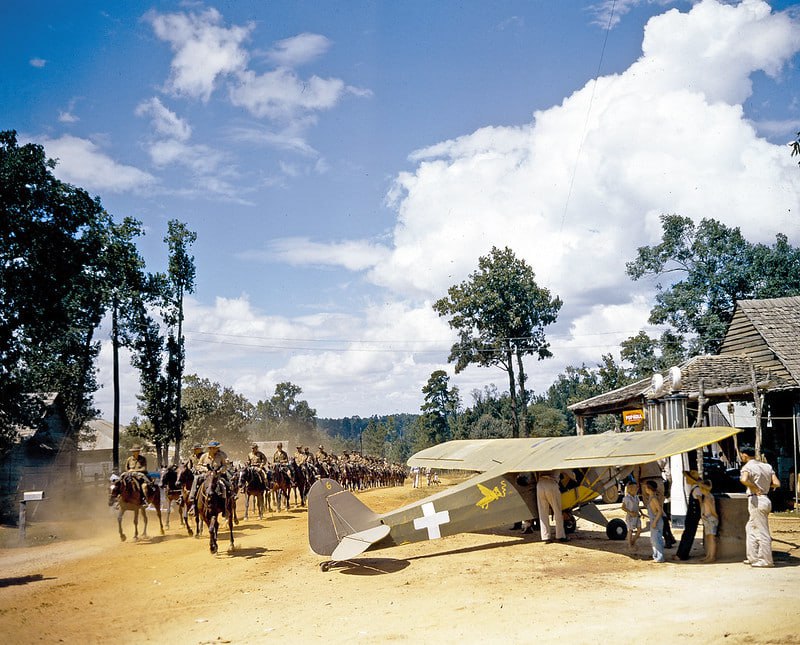 1941年路易斯安那演习中，一个美国陆军骑兵中队从一架Piper Cub飞机旁小跑而过