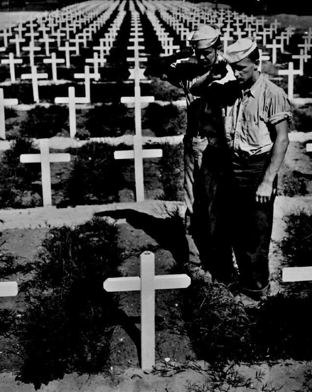 站在美军墓地的草坪上，旁边是一排排白色十字架，两名身着工装裤的海岸警卫队队员在悼念一位在琉球群岛阵亡的海岸警卫队队员