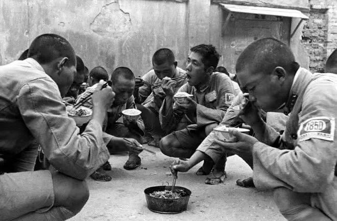 1939年3月25日，南昌会战期间，国民革命军第一八五师的士兵们着短裤、草鞋，在蹲着吃晚饭