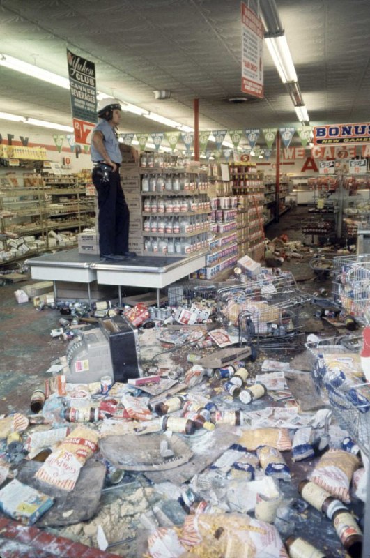 1967 年 ，一名底特律警察守卫着一家在种族骚乱中被抢劫的杂货店