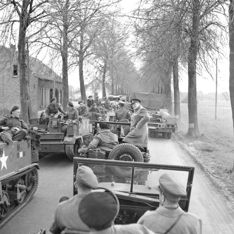 1945 年 3 月 26 日，在萊茵河進攻行動視察期間，英國首相溫斯頓·邱吉爾和陸軍元帥伯納德·蒙哥馬利停下吉普車，讓部隊乘坐運兵車通過